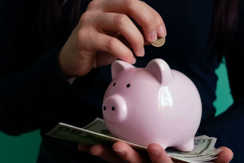 Person dividing money between savings account and CD using calculator and financial notes on desk.