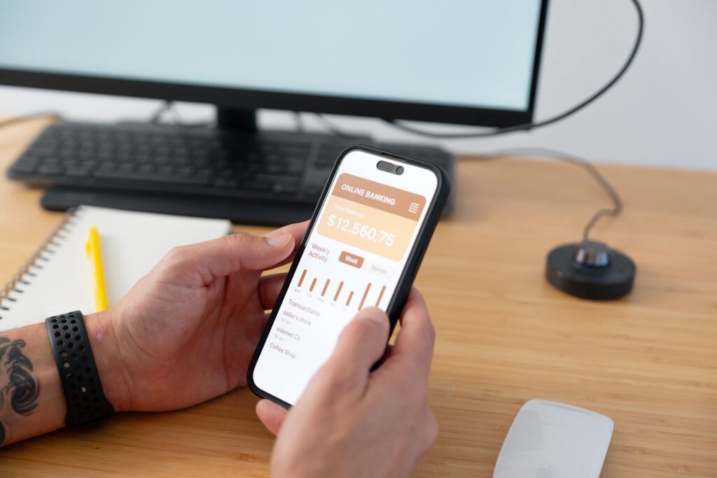 Person checking savings account balance on mobile with calculator and notes on desk.