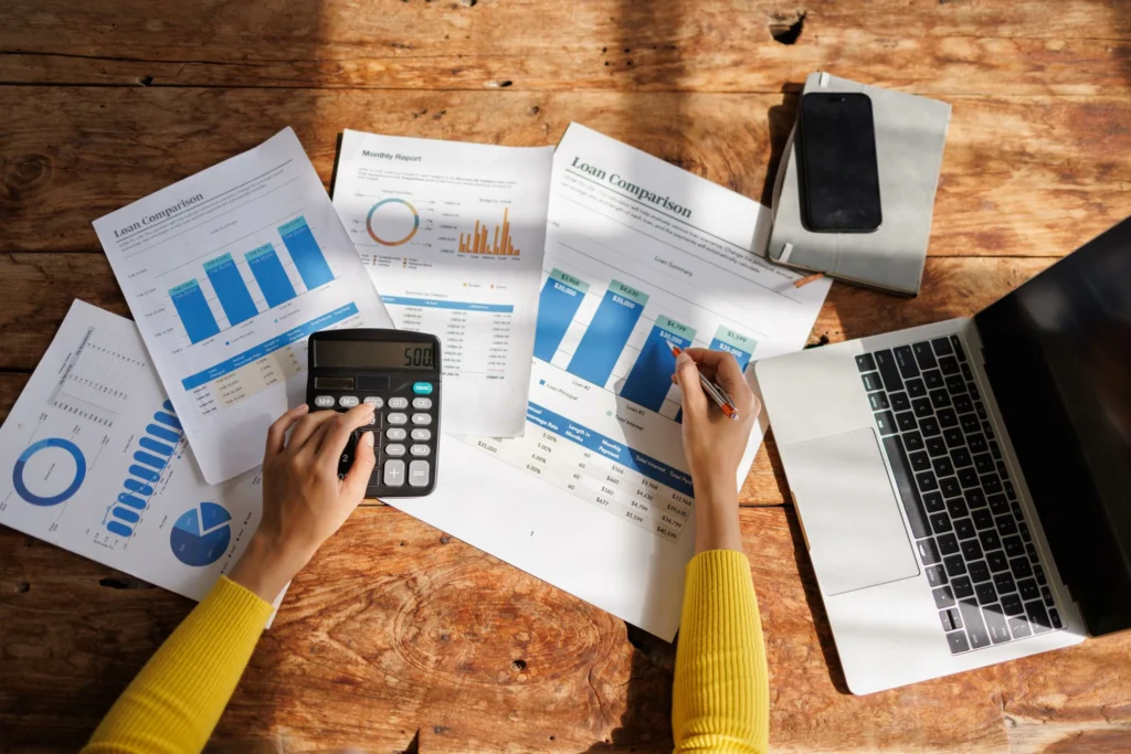 Person comparing CD and savings account returns using calculator and financial charts on a modern desk.